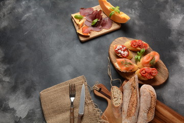 Brushetta or traditional Spanish tapas. Appetizers with Italian antipasti snacks. Variety of small sandwiches with cherry tomatoes, salmon, cream cheese. Prosciutto served with melon and basil