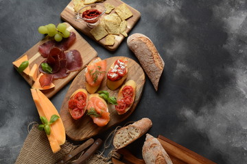 Brushetta or traditional Spanish tapas. Appetizers with Italian antipasti snacks. Variety of small sandwiches with cherry tomatoes, salmon, cream cheese. Prosciutto served with melon and basil