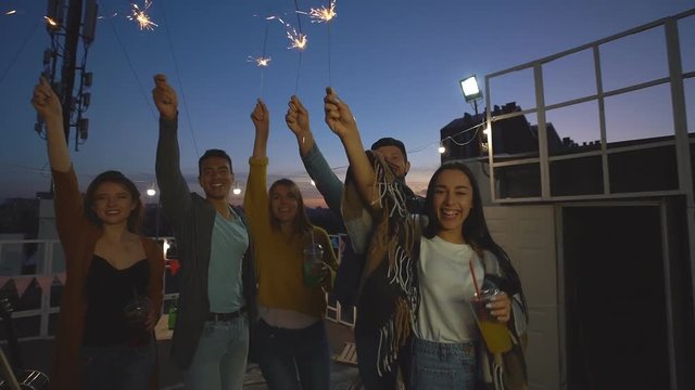 A group of friends waving sparklers and enjoying a party at night on the roof.