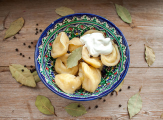 Dumplings with potato or meet served with butter or sour cream in dish on rustic wooden background