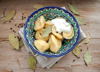 Dumplings with potato or meet served with butter or sour cream in dish on rustic wooden background