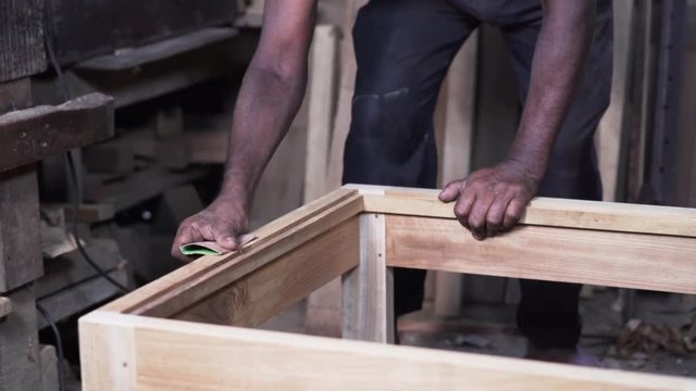 Working man is polishing a piece of wood with a sandpaper for grinding in a workshop
