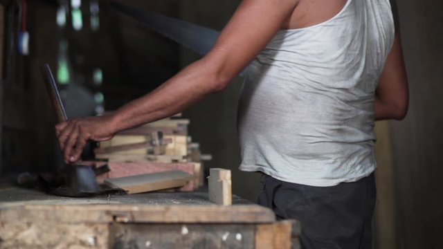 An adult man precisely sawing a wooden piece
