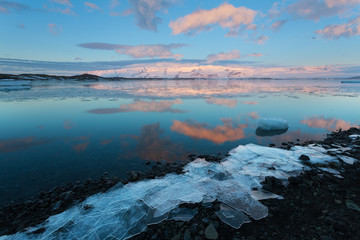 Icebergs float on Jokulsarlon glacier lagoon at sunrise, with background mountain peaks lit by sunrise, in Iceland.