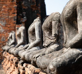 Fototapeta na wymiar Close up of ancient stone buddha statues placed in line in the ruined temple at Ayutthaya