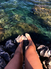 Woman feet sitting on rock above clear water