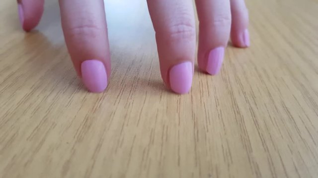 Female hand with white skin and pink short nails scratching a wooden table like cat, close-up