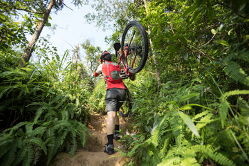 Woman cyclist carry a mountain bike walking on tropical forest trail