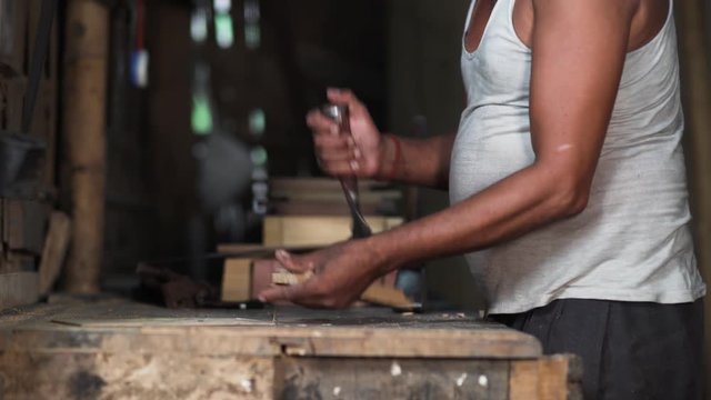Side view of a carpenter using a chisel on a small wooden part