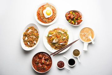 Assorted Indo chinese food in group includes non vegetarian or chicken Schezwan/Szechuan hakka noodles, fried rice, manchurian, egg american chop suey, soup with spoon and chop sticks, selective focus