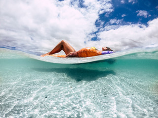 Beautiful tanned young woman lay down and relax on a trendy inflatable lilo in a paradise beach with sand and clear blue water - underwater and out image for vacation and travel concept lifestyle