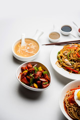 Assorted Indo chinese food in group includes non vegetarian or chicken Schezwan/Szechuan hakka noodles, fried rice, manchurian, egg american chop suey, soup with spoon and chop sticks, selective focus