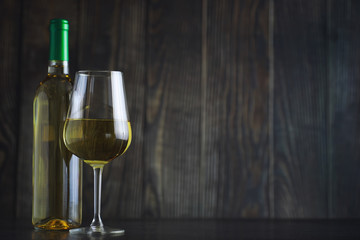 Transparent bottle of white dry wine on the table. White wine glass on a wooden background.