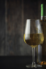 Transparent bottle of white dry wine on the table. White wine glass on a wooden background.