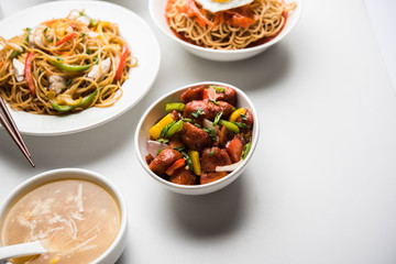 Assorted Indo chinese food in group includes non vegetarian or chicken Schezwan/Szechuan hakka noodles, fried rice, manchurian, egg american chop suey, soup with spoon and chop sticks, selective focus