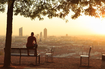 Man on a bench relaxing and enjoying the summer sunrise over a city. Lyon, France.