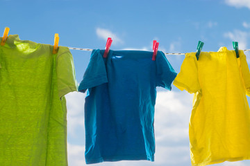 Multicolored bright clothes are drying on a rope against the blue sky with 