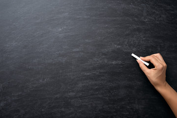 Education or back to school Concept. Woman hand holding chalk over chalkboard background.