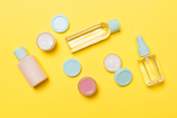 Set of travel size cosmetic bottles on yellow background. Flat lay of cream jars. Top view of bodycare style concept