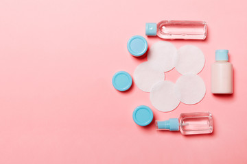 Group of small bottles for travelling on pink background. Copy space for your ideas. Flat lay composition of cosmetic products. Top view of cream containers with cotton pads