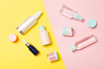 Top view of different cosmetic bottles and container for cosmetics on pink and yellow background. Flat lay composition with copy space