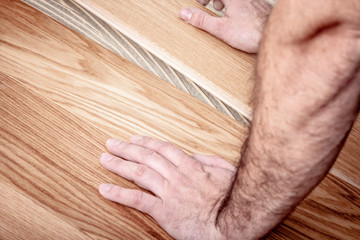 Handwerker verlegt Parkettboden und streicht den Estrich mit Kleber ein und schlägt die Dielen mit...