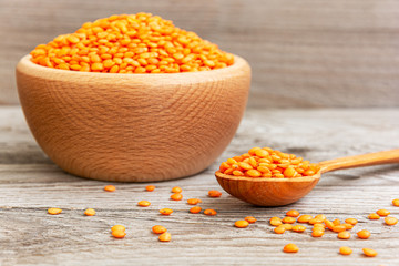 Photo of red lentils in wooden bowl with spoon on wooden background. Product photo of red lentils. Healthy lifestyle. Vegetarian and vegan diet. Spilled lens