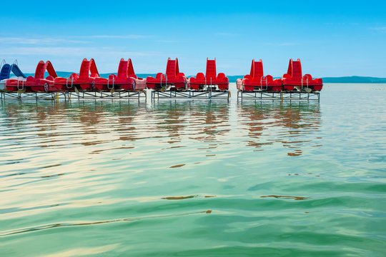 Travel background of red pedal boats on a pier with big water surface in the front at lake Balaton in Hungary