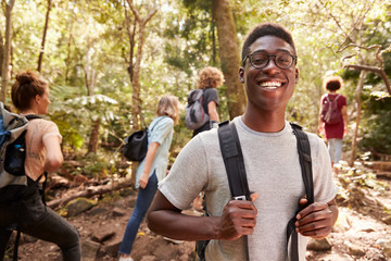 Waist up portrait of smiling millennial African American man hiking in a forest with friends, close...