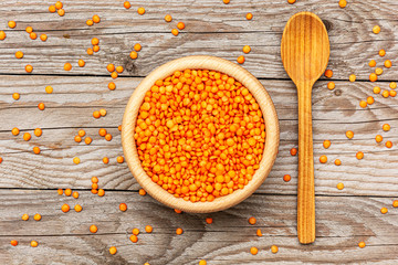 Flat lay photo of red lentils in wooden bowl with spoon on wooden background. Product photo of red lentils. Healthy lifestyle. Vegetarian and vegan diet. Spilled lens
