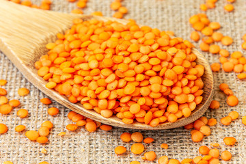 Red lentils in a wooden spoon on a background of burlap. Product photo of red lentils. Healthy lifestyle. Vegetarian and vegan diet. Spilled lens