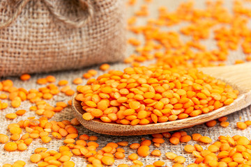Red lentils in a wooden spoon on a background of burlap. Product photo of red lentils. Healthy lifestyle. Vegetarian and vegan diet. Spilled lens