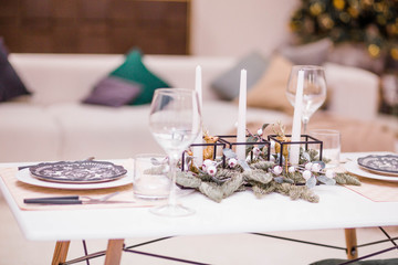 Table setting in the New Year's style. Christmas tree branches, candles and deer figurines as decor