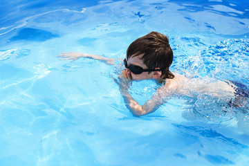 boy dives in swimming pool with swimming glasses. boy swims in the pool. child learning to swim