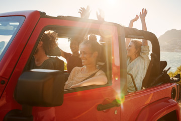 Excited young adult friends on a road trip vacation driving in an open top car, lens flare