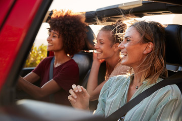 Three millennial female friends on a road trip driving together in an open jeep, close up