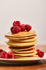 selective focus of tasty pancakes with raspberries on plate isolated on grey