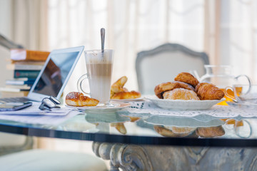 Home office, ideal working environment with breakfast. Luxury interior, glass table, reflection, notebook, eyeglasses, mobile phone and blurred background. Wellbeing at work.