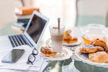 Home office, ideal working environment with breakfast. Luxury interior, glass table, reflection, notebook, eyeglasses, mobile phone and blurred background. Wellbeing at work.