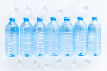 Plastic bottles with pure water and ice on white background top view