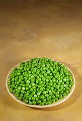 Green peas on a plate standing on the table top of yellow marble.