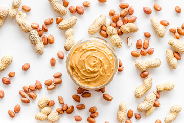 Product for hearty breakfast with peanut butter in bowl near nuts on white background top view...