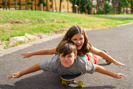 Brother and sister playing with skateboard. Little boy and girl on longboard skate in the park. Young in summer time.  Family and childhood concept. Focus the faces. Image