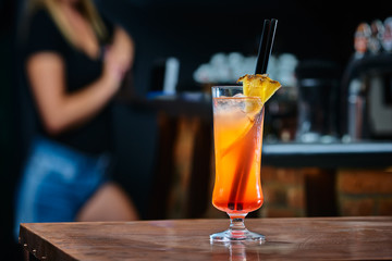 Drink with pinapple in a night bar. Blurred woman in the background. Selective focus on the icy drink. Copy space