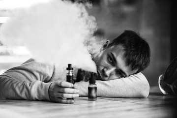 Vape man. Indoor portrait of a young handsome white caucasian guy letting puffs of steam from an...