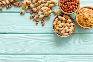 Product for hearty breakfast with peanut butter in bowl near nuts on mint green wooden background top view mockup