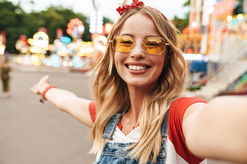 Cheerful happy young blonde woman in amusement park prendre selfie par caméra.