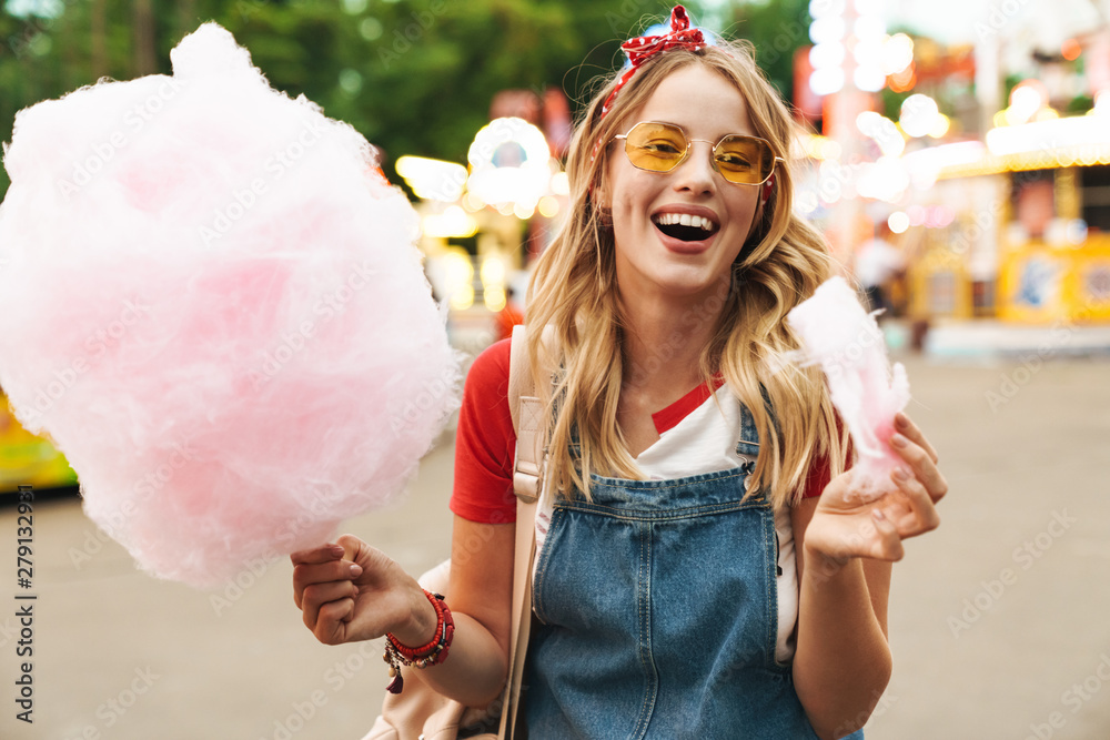 Wall mural Laughing young blonde woman in amusement park holding cotton candy candyfloss.