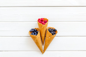 Fresh berries in waffle cones on white wooden background top view