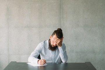 Obraz premium Resignation notice. Tired bearded man writing formal letter. Gray wall background. Copy space.